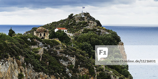 Haus und altes Gebäude mit griechischer Flagge auf einer felsigen Landzunge am Ägäischen Meer; Skiathos  Griechenland'.