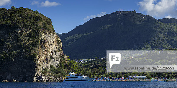A yacht beside a tall cliff and mountainous landscape on the island of Ischia; Ischia  Campania  Italy