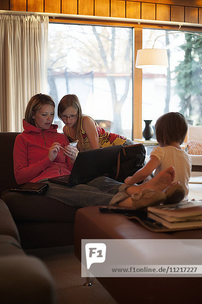 Mutter zu Hause mit Töchtern  die ein Mobiltelefon und einen Laptop benutzen; Regina  Saskatchewan  Kanada