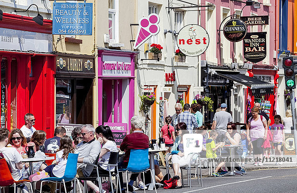 Kunden sitzen an Tischen auf der Straße vor Geschäften; Kenmare  County Kerry  Irland