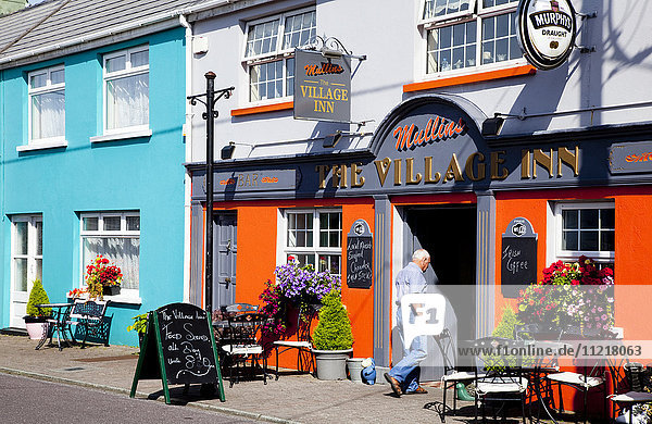 Senior man walking into Village Inn and colourful buildings along the street; Ardgroom  County Cork  Ireland