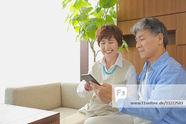 Modisches japanisches Seniorenpaar mit Tablet auf dem Sofa