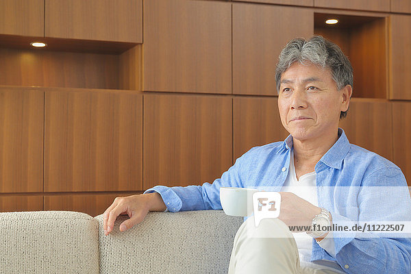 Fashionable Japanese senior man having a cup of coffee on the sofa