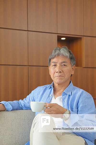 Modischer japanischer älterer Mann mit einer Tasse Kaffee auf dem Sofa