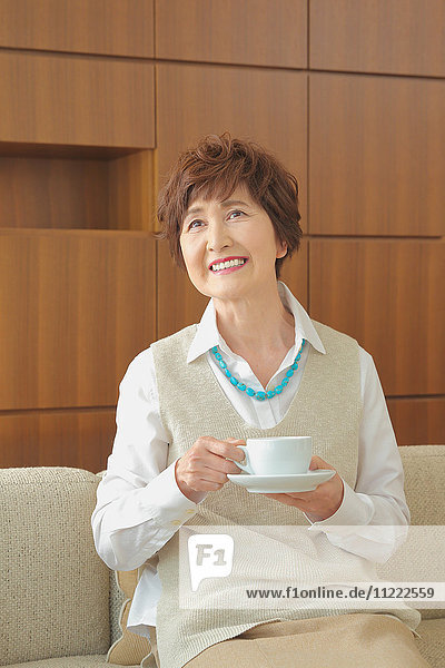 Fashionable Japanese senior woman having a cup of coffee on the sofa