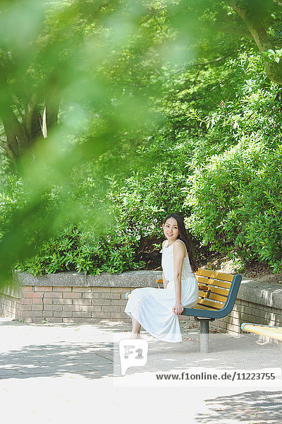 Junge japanische Frau sitzt auf einer Bank in einem Stadtpark
