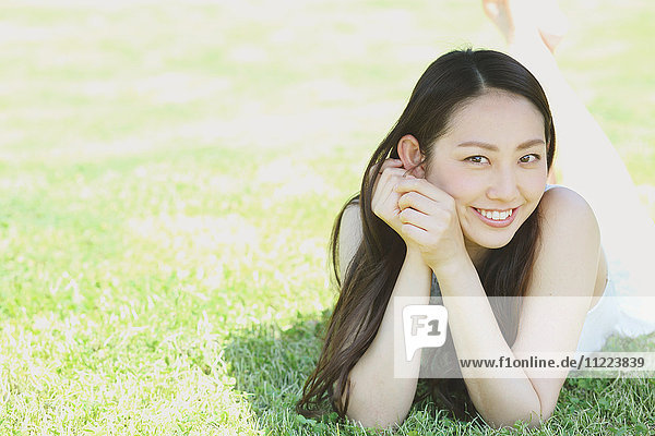 Porträt einer jungen japanischen Frau  die auf grünem Gras liegt