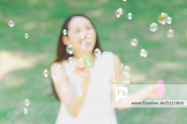 Junge Japanerin bläst Seifenblasen in einem Stadtpark