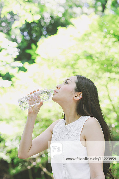 Junge Japanerin trinkt Wasser in einem Stadtpark