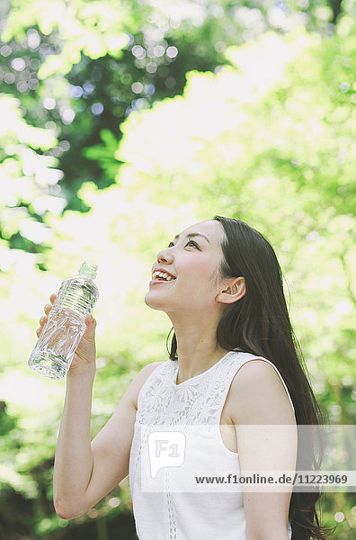 Junge Japanerin trinkt Wasser in einem Stadtpark