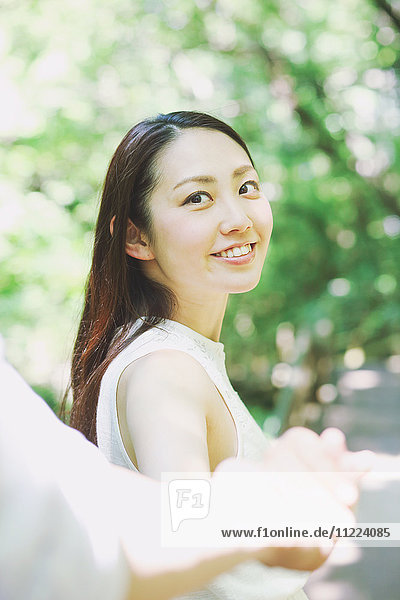Junge japanische Frau hält die Hand eines Mannes und lächelt in einem Stadtpark