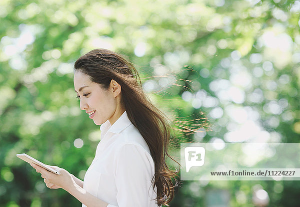 Young Japanese woman with tablet surrounded by green in a city park