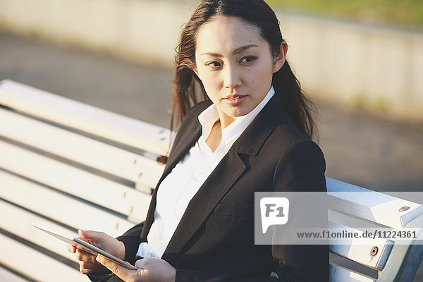Junge japanische Geschäftsfrau mit Tablet an einem Fluss in der Innenstadt von Tokio