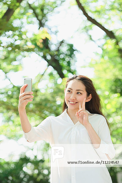 Junge japanische Frau nimmt Selfie umgeben von Grün in einem Stadtpark