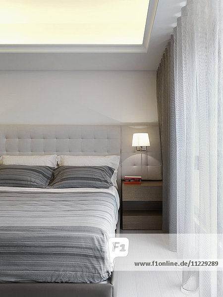 Bett mit grau gestreiften Laken in einem modernen Schlafzimmer