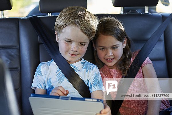 Brother and sister in car using tablet