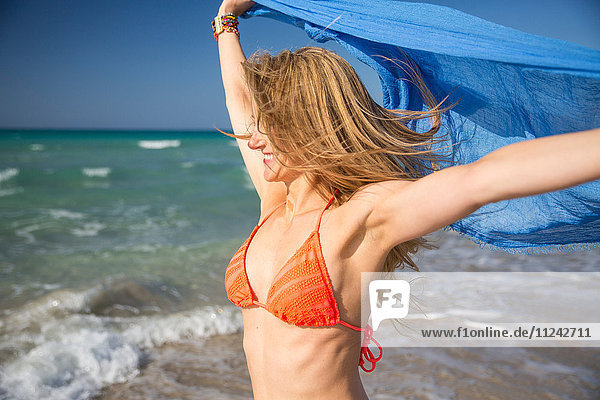 Frau hält Schal am Strand hoch