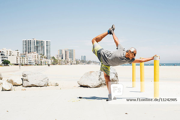 Senior man  exercising on beach  stretching leg  Long Beach  California  USA