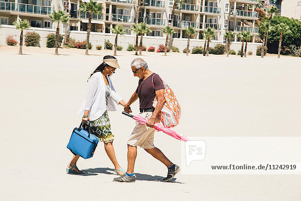 Senior couple walking on beach  carrying bags for picnic  Long Beach  California  USA
