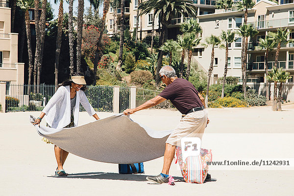 Senior couple on beach  laying out blanket for picnic  Long Beach  California  USA