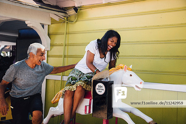 Senior woman on horse funfair ride  senior man standing beside her  laughing  Long Beach  California  USA