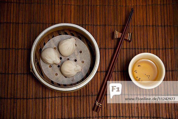 Asiatische Knödel  Tee und Essstäbchen auf Bambusmatte