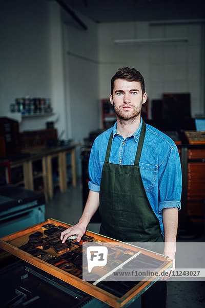 Porträt eines jungen Handwerkers neben dem Tablett mit Buchdruckbuchstaben in der Druckwerkstatt