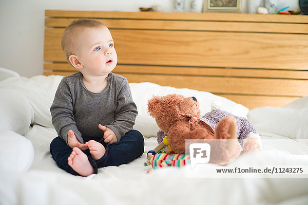 Kleines Mädchen sitzt auf dem Bett mit Teddybär,  der wegschaut