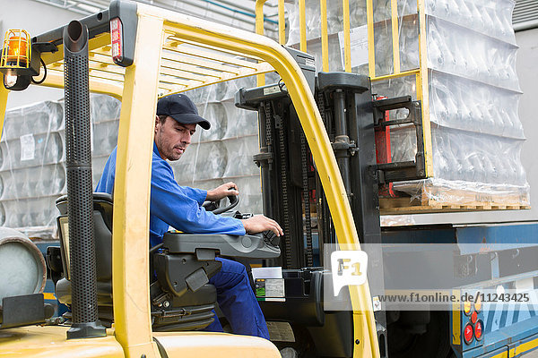 Forklift driver loading pallet onto truck at packaging factory