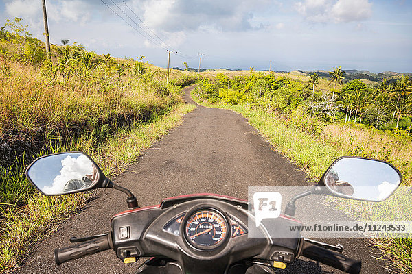 Mirror image of motorcyclist in motorcycle wing mirrors on rural road Tanglad Nusa Penida Indonesia