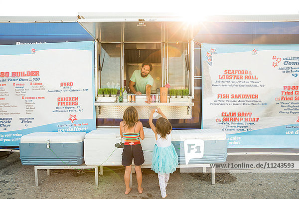 Mann in Fast-Food-Wohnwagen serviert zwei junge Mädchen neben einem Wohnwagen