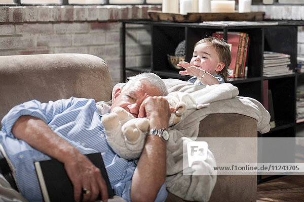 Baby Mädchen berührt schlafenden Großvater auf der Couch