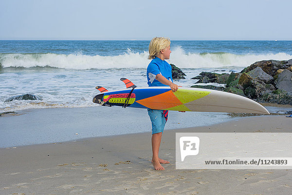 Junge am Strand  der ein Surfbrett hält
