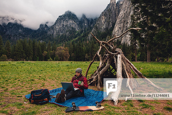 Wanderer  der mit einem Laptop an einer Höhle sitzt  Yosemite  Kalifornien  USA
