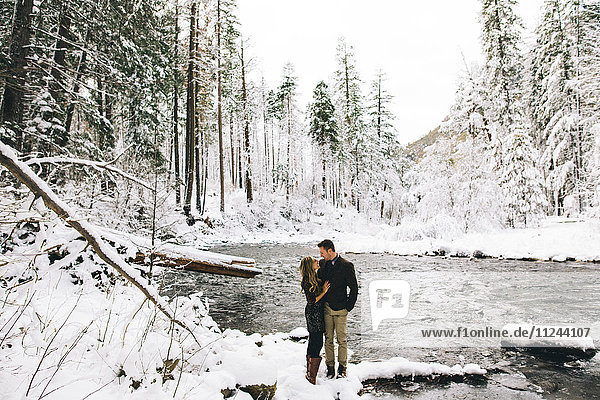 Lächelndes Paar im schneebedeckten Wald am Fluss