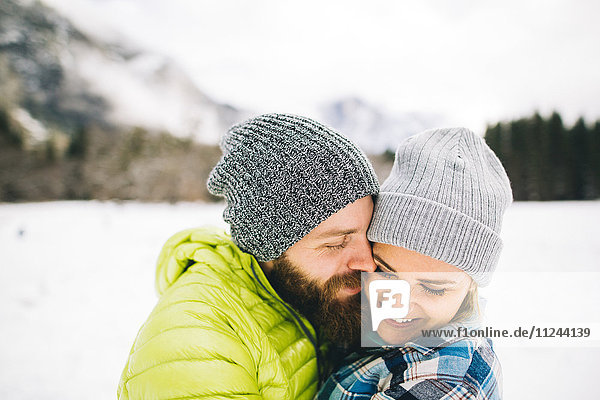 Couple on snow-covered landscape wearing knit hats hugging