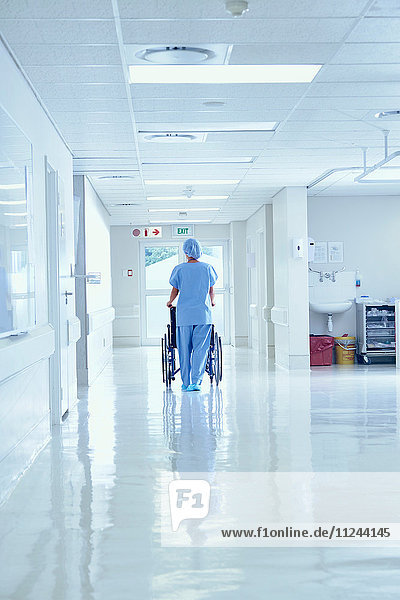 Rear view of nurse pushing wheelchair along hospital corridor