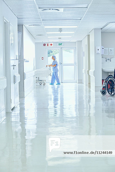 Female nurse pushing bed on hospital corridor