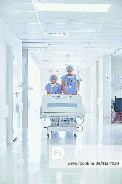Male and female nurses pushing patient bed on hospital corridor