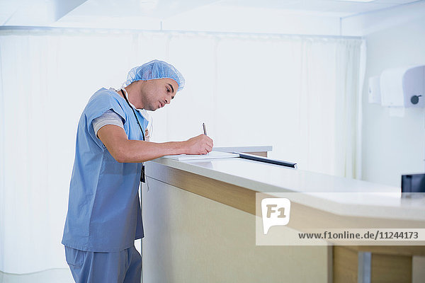 Männlicher Arzt schreibt medizinische Notizen auf der Schwesternstation im Krankenhaus