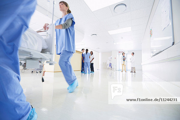 Male and female medics urgently pushing hospital bed along corridor