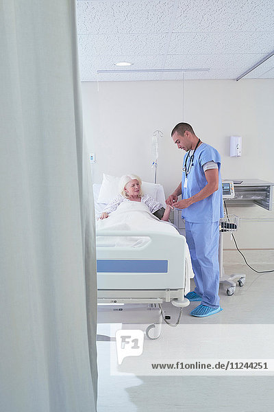 Male nurse using blood pressure gauge on senior female patient in hospital bed