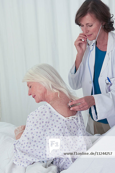 Ärztin  die einer älteren Patientin mit dem Stethoskop zuhört