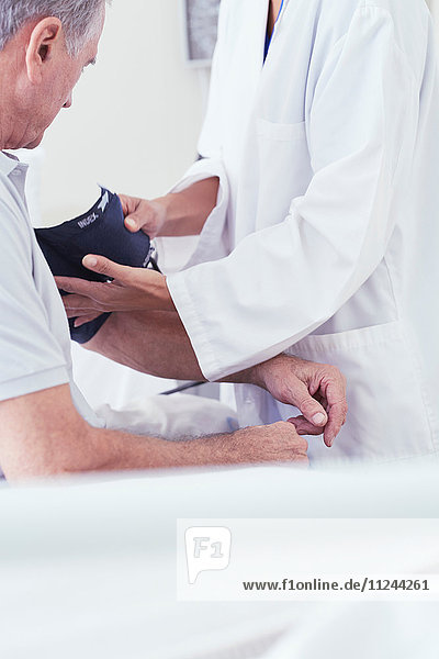 Schnappschuss einer Ärztin mit Blutdruckmesser bei einem älteren männlichen Patienten am Krankenhausbett