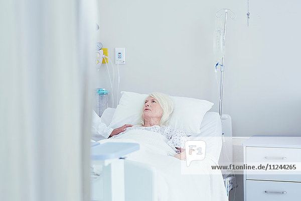 Arzt im Gespräch mit besorgter älterer Patientin im Krankenhausbett