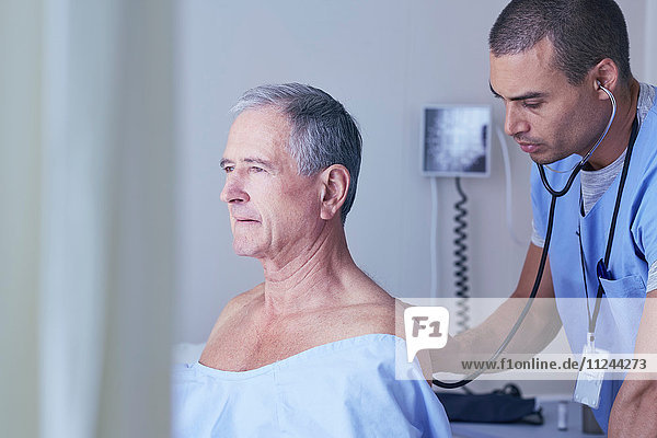Male nurse listening to senior male patient back with stethoscope