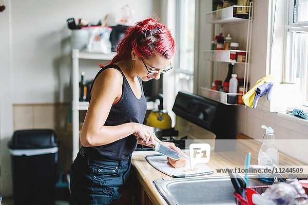 Junge Frau mit rosa Haaren schneidet Fleisch in der Küche