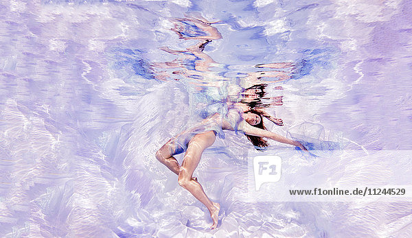 Underwater view of woman draped in sheer fabric  floating towards water surface