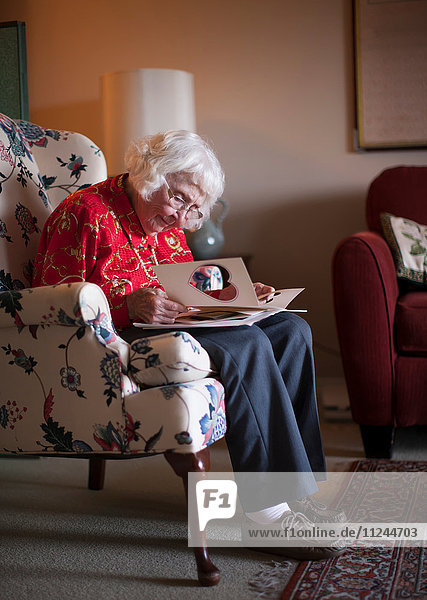 Ältere Frau sitzt auf einem Stuhl und schaut auf eine Grußkarte
