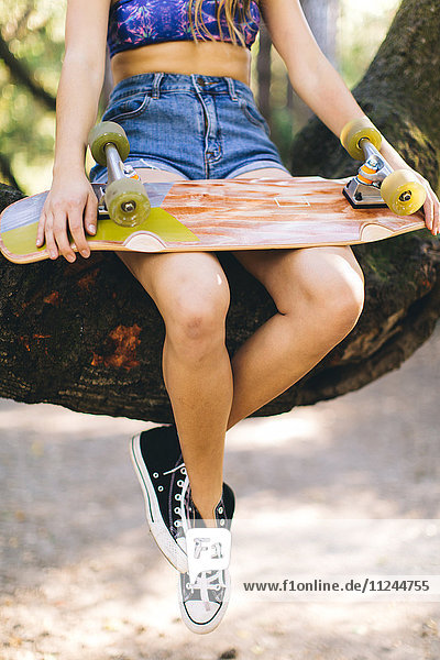 Frau mit Skateboard auf Baum sitzend